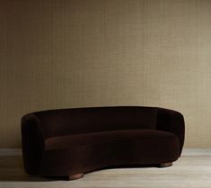 a brown couch sitting on top of a wooden floor next to a wall with beige walls