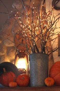 an arrangement of pumpkins and branches on a mantel with a lantern in the background