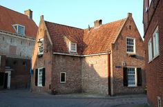 an old brick building with red tile on the roof and two storyed buildings behind it