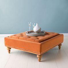 an orange ottoman sitting on top of a white floor next to a vase and two candles