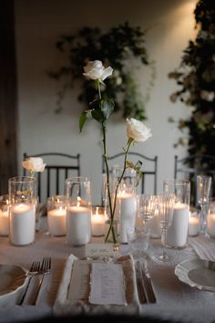 the table is set with white candles and flowers in vases, plates and napkins