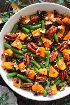 a white bowl filled with green beans, carrots and pecans