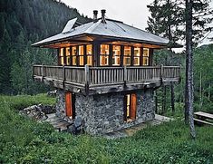 a small stone cabin in the woods with lights on and windows lit up at night