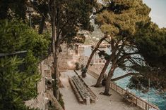 an outdoor seating area next to the water with trees on both sides and benches in front