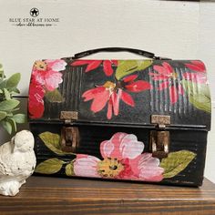 an old suitcase with flowers painted on it sitting next to a small white bird and potted plant