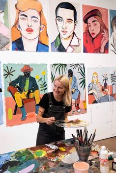 a woman standing in front of paintings on the wall and holding a tray with paint