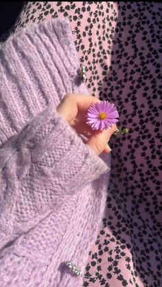 a person holding a flower in their left hand and wearing a sweater on the other