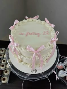 a large white cake with pink bows on it's side and some cookies in the background