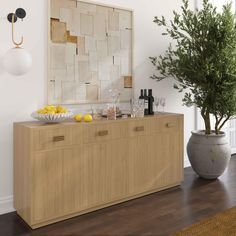 a wooden buffet table sitting next to a potted plant on top of a hard wood floor