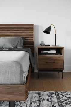 a bed sitting next to a night stand on top of a wooden floor