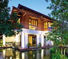 a large house sitting next to a body of water in front of a lush green forest