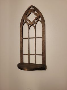 a wooden shelf with an arched window on the wall in front of a white wall