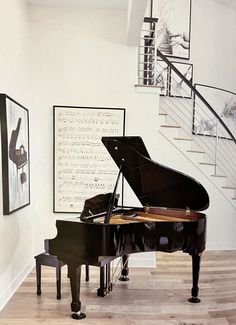 a grand piano sits in the middle of a room with stairs and pictures on the wall