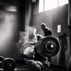 a black and white photo of a man lifting a barbell in front of a mirror