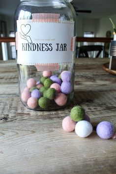 a jar filled with colorful pom poms sitting on top of a wooden table