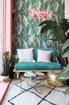 a living room with green couches, pink pillows and monster leaves on the wall