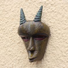 a close up of a mask with horns on it's head against a wall