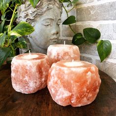 three candles sitting on top of a wooden table next to a statue and potted plant