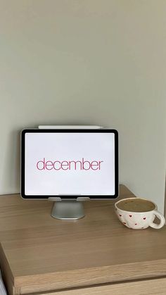 a computer monitor sitting on top of a wooden desk next to a cup of coffee