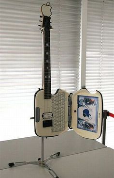 a guitar shaped like an apple computer sitting on top of a table next to a window