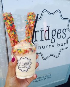 a person holding up a drink in front of a sign that reads bridge's churro bar