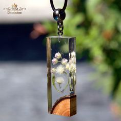 a glass block with flowers in it hanging from a black cord on a wooden piece