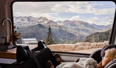 a baby in a car seat looking out the window at mountains