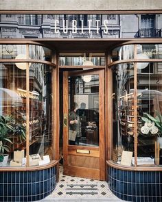 the front entrance to a store with large windows and plants in pots on display outside