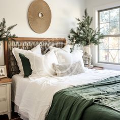 a bed with white sheets and green pillows in a bedroom next to a christmas tree