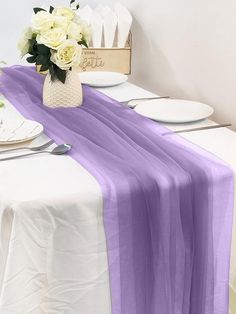 the table is set with white plates and silverware, along with a purple runner