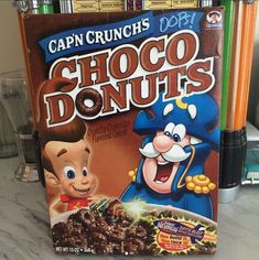 a box of chocolate donuts sitting on top of a counter next to some pencils