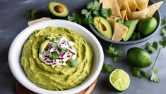 a white bowl filled with guacamole surrounded by tortilla chips and limes