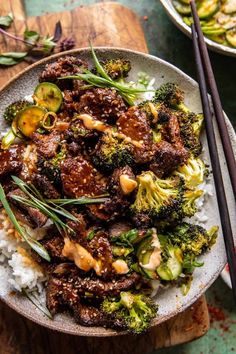 beef and broccoli stir fry on rice with chopsticks next to it