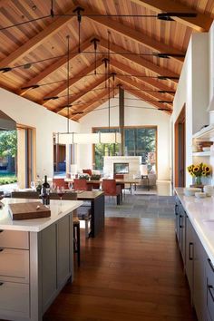 an open kitchen and living room with wooden ceilings, white counter tops and wood flooring