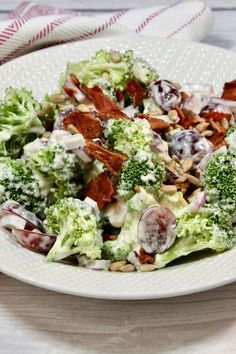 a white plate topped with broccoli salad covered in cheese and bacon dressing on top of a wooden table