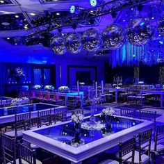 a room filled with lots of tables covered in blue lights and chandelier hanging from the ceiling