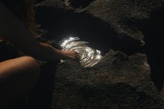 a person kneeling down in the dirt with their hand on a glass object that is glowing