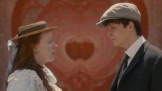 a man and woman standing next to each other in front of a red wall wearing hats