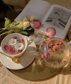 a table topped with flowers next to an open book and tea pot on top of a plate