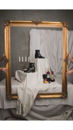 a person holding up a large mirror with shoes and candles on it in front of them