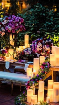 a table with candles and flowers on it in the middle of a garden at night