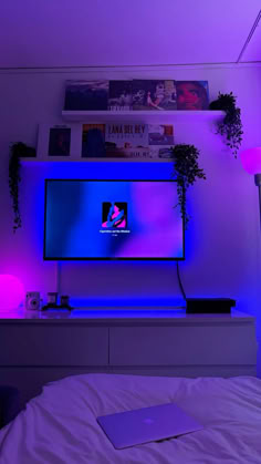 a flat screen tv sitting on top of a white dresser next to a purple light