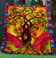 the tree of life quilt is on display in front of some trees and grass with colorful colors