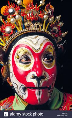 a man with painted face and headdress, wearing a red and white mask - stock image