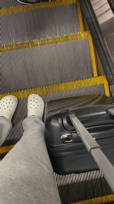 a person's feet sticking out of an escalator next to a suit case