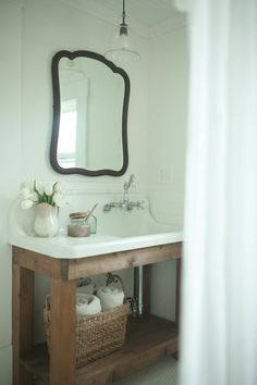 a white sink sitting under a bathroom mirror next to a wooden table with baskets on it