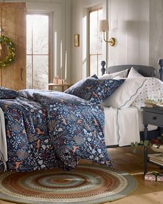 a bed with blue and white comforters in a room next to a table, christmas wreath on the wall