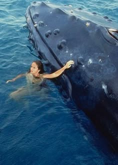 a woman is swimming in the water next to a large object that looks like a submarine