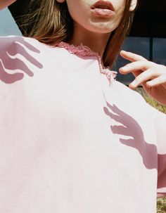 a woman in a pink top is holding her hand up to her head and looking at the camera