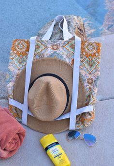 a hat, sunglasses and sunscreen are sitting on the ground next to a beach bag